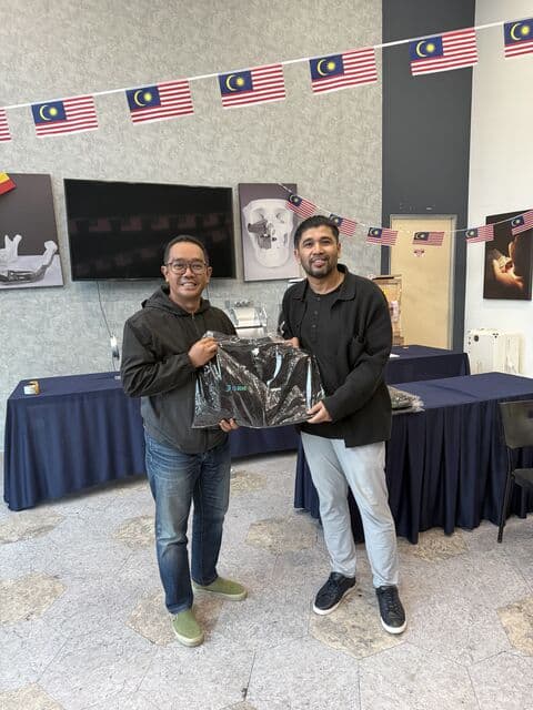 Team member in a dark jacket receives a 3D Gens bomber jacket