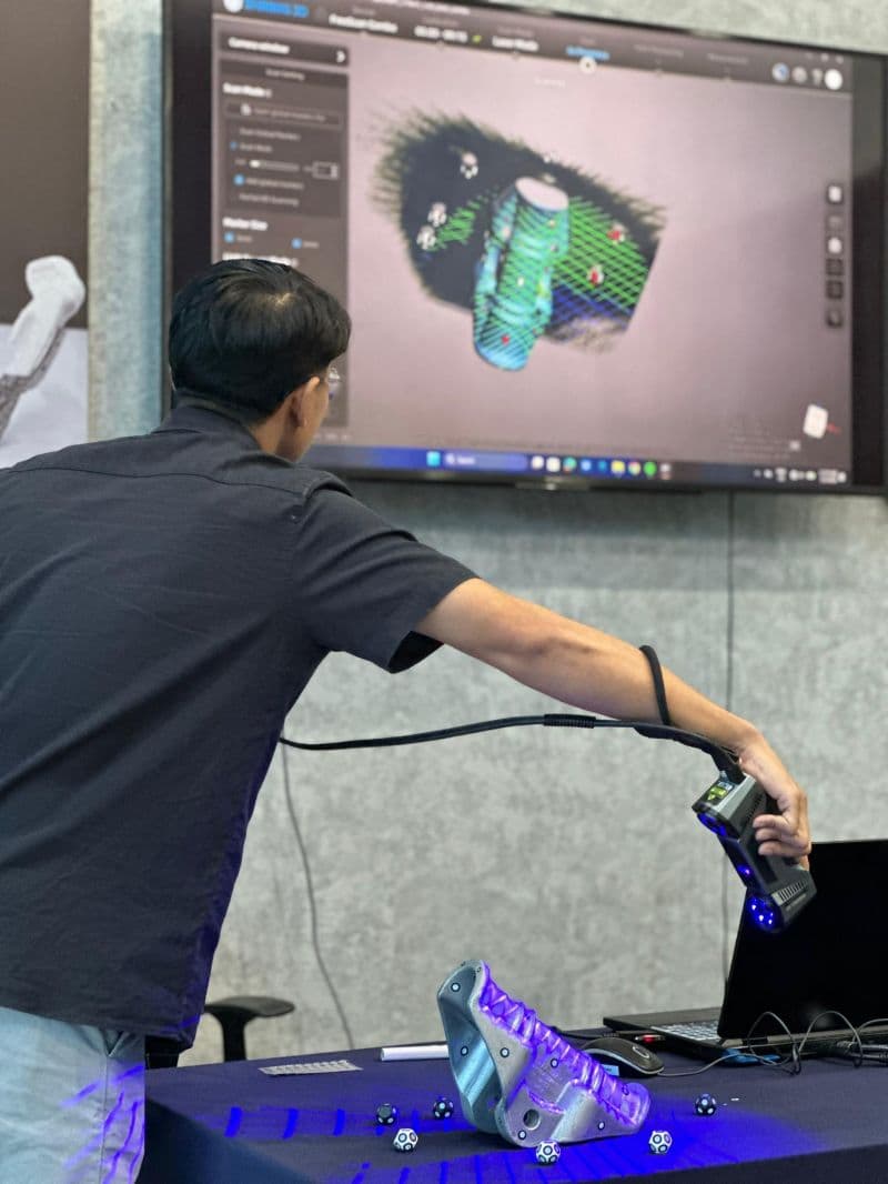 Close-up of a 3D Gens engineer scanning a metal additive manufactured part with a structured-light 3D scanner, showing the resulting point cloud on a large display